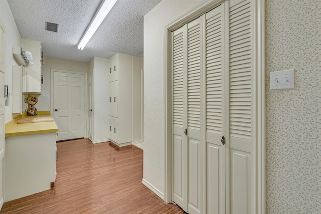 corridor with a textured ceiling and light hardwood / wood-style flooring