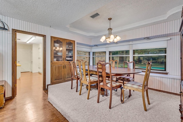 dining room with a chandelier, a raised ceiling, light hardwood / wood-style floors, and a textured ceiling