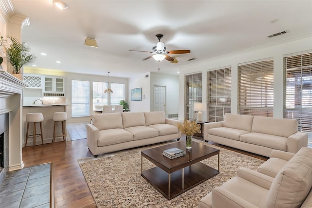 living room with dark wood-type flooring, sink, ceiling fan, ornamental molding, and a fireplace