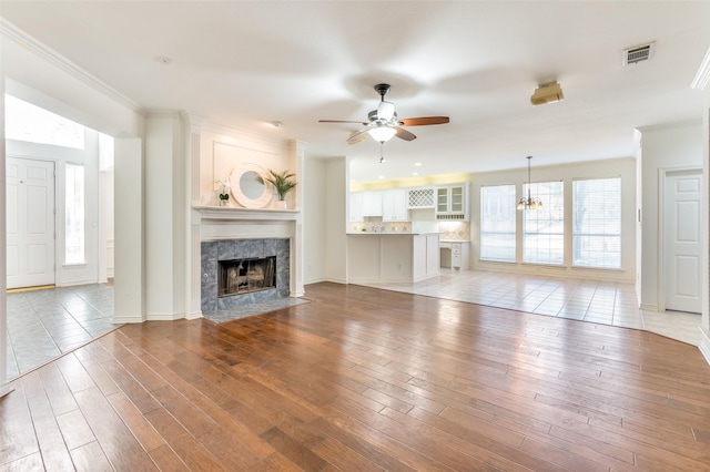 unfurnished living room with light wood-type flooring, plenty of natural light, ornamental molding, and a tiled fireplace