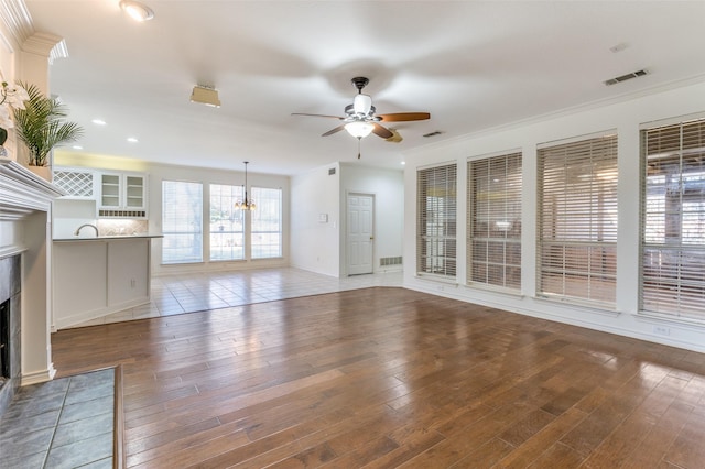 unfurnished living room featuring a tile fireplace, sink, wood-type flooring, ceiling fan with notable chandelier, and ornamental molding