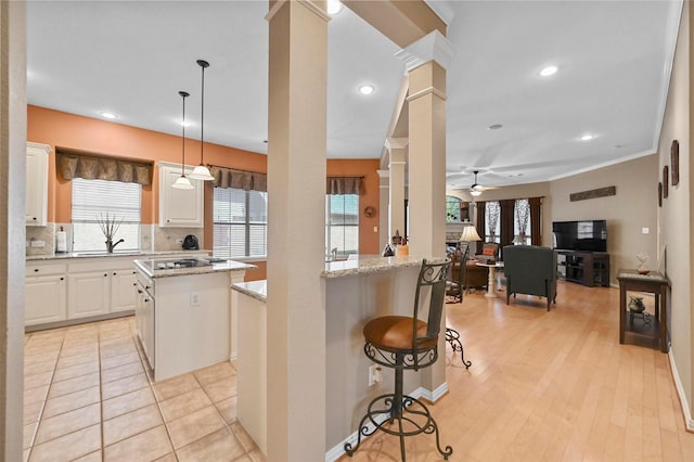 kitchen featuring pendant lighting, a breakfast bar, decorative columns, light stone counters, and a kitchen island