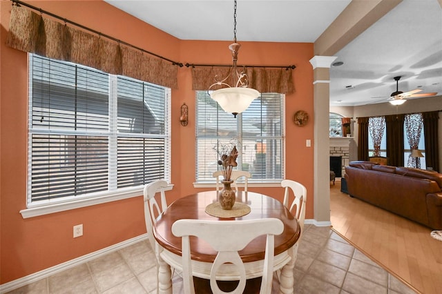 tiled dining space with a fireplace, ceiling fan, and ornate columns