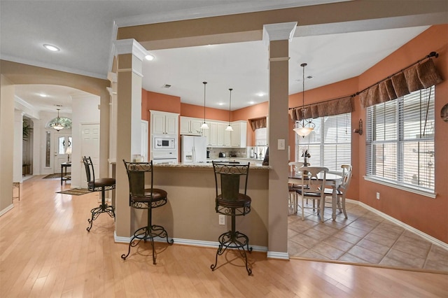 kitchen with a breakfast bar, decorative light fixtures, light stone counters, kitchen peninsula, and white appliances