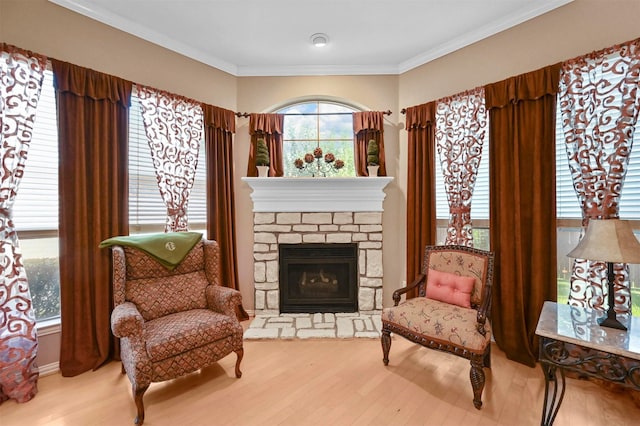 living area with crown molding, wood-type flooring, and a stone fireplace