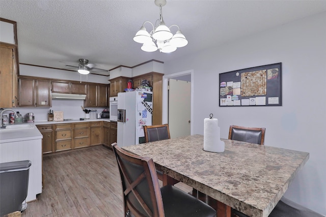 kitchen featuring white appliances, sink, light hardwood / wood-style flooring, a kitchen bar, and decorative light fixtures