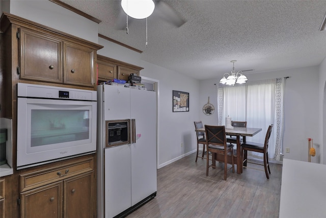 kitchen featuring light wood-type flooring, white appliances, ceiling fan with notable chandelier, hanging light fixtures, and a textured ceiling