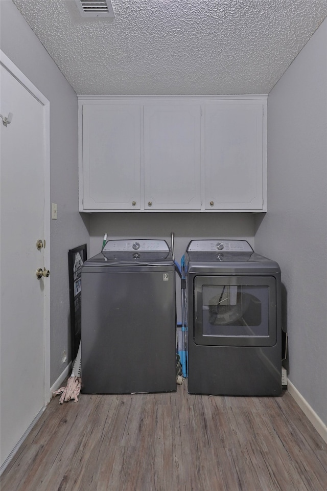 clothes washing area with washer and clothes dryer, cabinets, light hardwood / wood-style flooring, and a textured ceiling