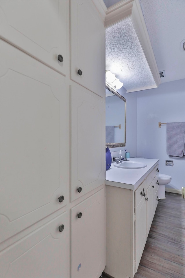 bathroom with a textured ceiling, hardwood / wood-style flooring, vanity, and toilet