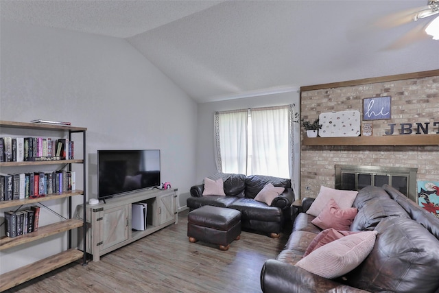 living room with a brick fireplace, lofted ceiling, ceiling fan, and light hardwood / wood-style flooring