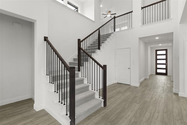 stairs with a high ceiling, wood-type flooring, and ceiling fan