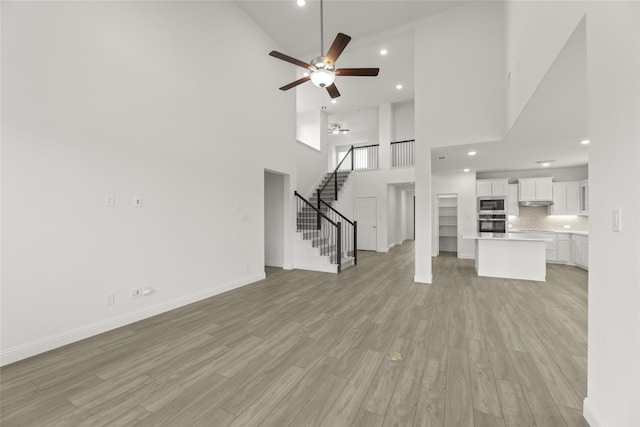 unfurnished living room with high vaulted ceiling, ceiling fan, and light wood-type flooring