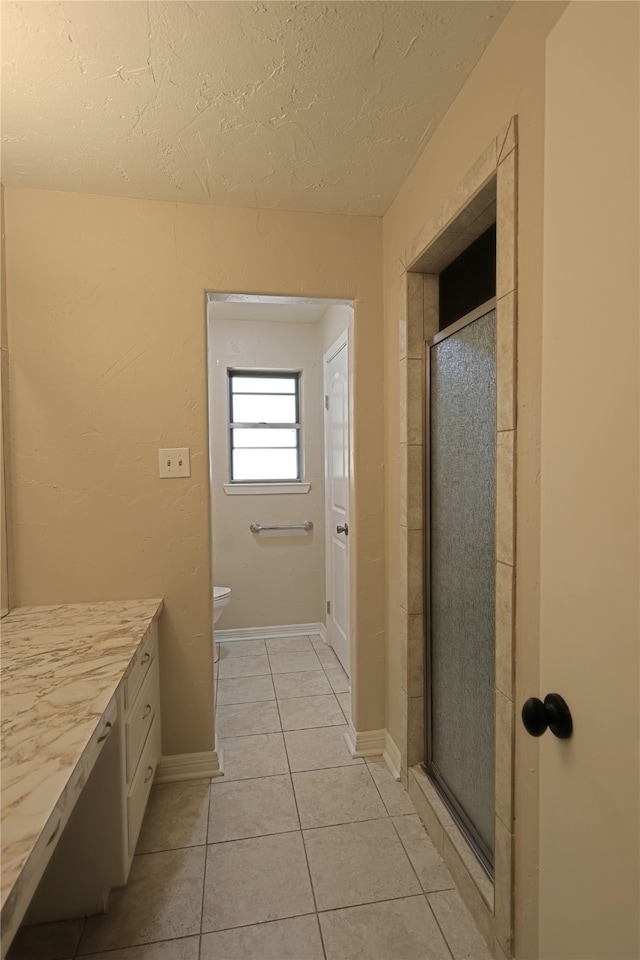 bathroom with a textured ceiling, tile patterned flooring, vanity, toilet, and walk in shower