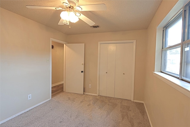 unfurnished bedroom featuring ceiling fan, light colored carpet, a textured ceiling, and a closet