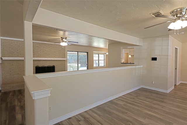 unfurnished living room with ceiling fan, a brick fireplace, brick wall, and hardwood / wood-style floors