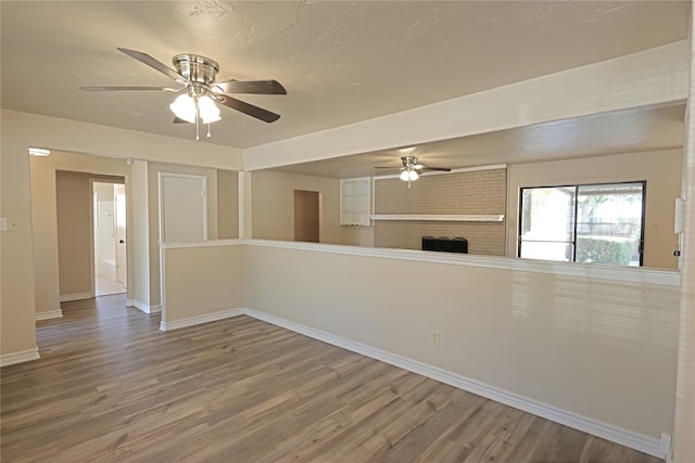 unfurnished room featuring ceiling fan, a fireplace, and wood-type flooring