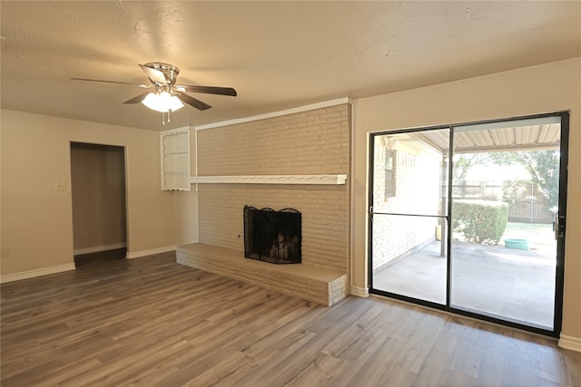 unfurnished living room with a textured ceiling, ceiling fan, wood-type flooring, and a brick fireplace