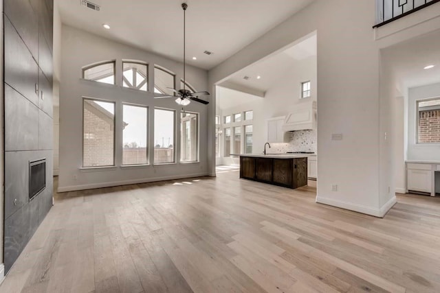 unfurnished living room featuring ceiling fan, a tile fireplace, sink, a high ceiling, and light wood-type flooring