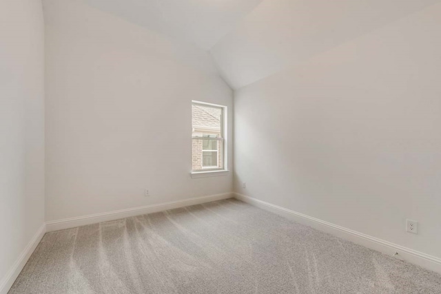 carpeted spare room with vaulted ceiling