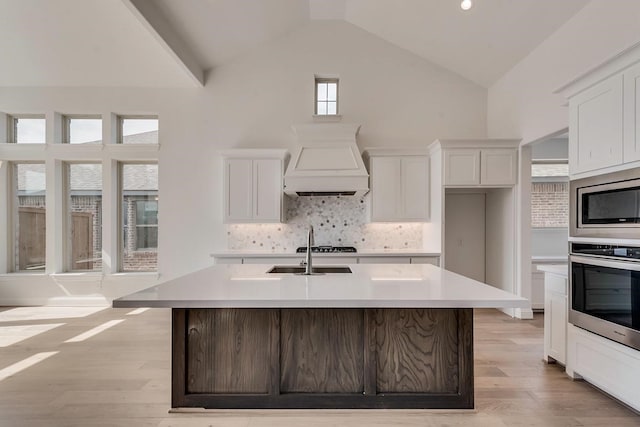 kitchen featuring stainless steel appliances, decorative backsplash, a kitchen island with sink, lofted ceiling, and white cabinets