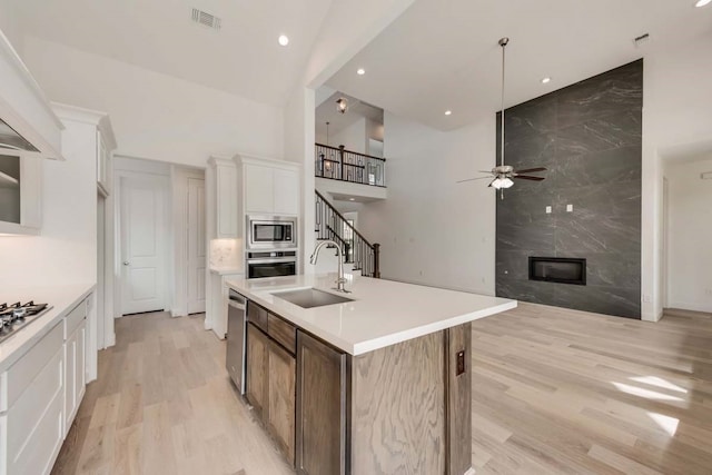 kitchen with white cabinetry, an island with sink, stainless steel appliances, a high end fireplace, and sink