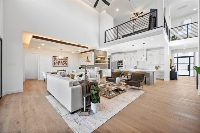 living area with ceiling fan with notable chandelier, a high ceiling, visible vents, baseboards, and light wood-style floors