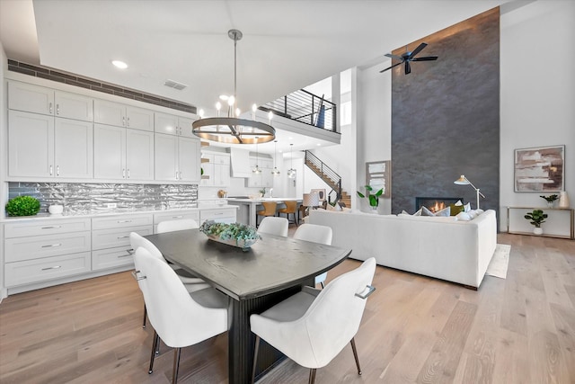 dining room with a large fireplace, light wood finished floors, a high ceiling, and visible vents