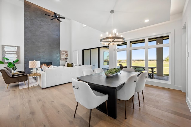 dining space with a high ceiling, an inviting chandelier, light wood-style floors, an accent wall, and a large fireplace