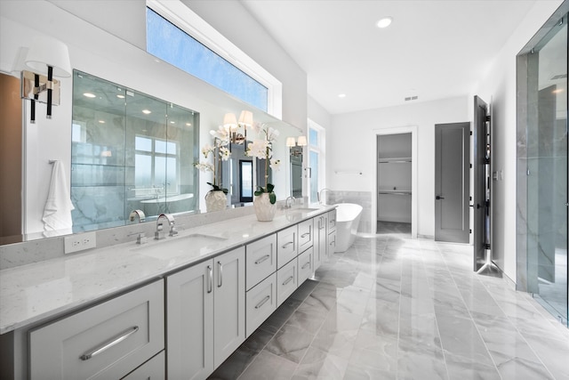 bathroom featuring double vanity, marble finish floor, a freestanding tub, and a sink