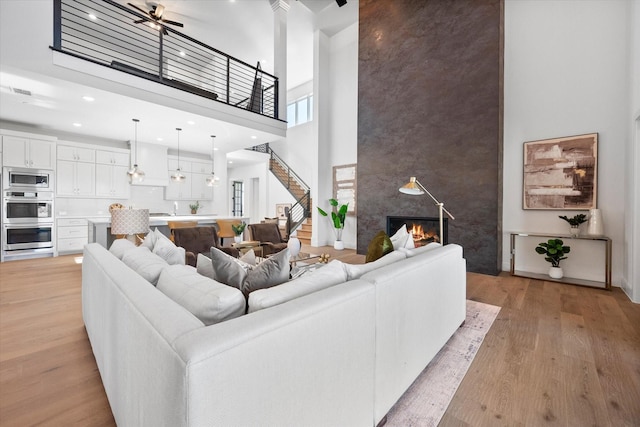 living area featuring a towering ceiling, light wood-style flooring, an accent wall, stairway, and a fireplace