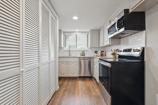 kitchen with appliances with stainless steel finishes, wood finished floors, light countertops, white cabinetry, and a sink