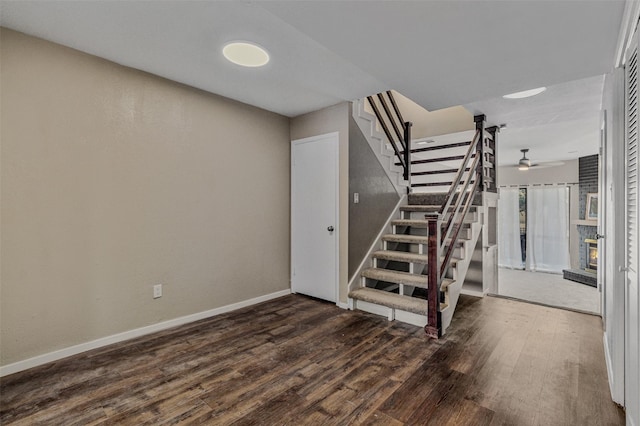 staircase featuring a brick fireplace, wood-type flooring, and ceiling fan