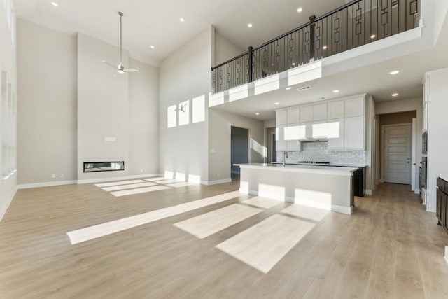 kitchen featuring light wood-style floors, open floor plan, white cabinets, an island with sink, and baseboards