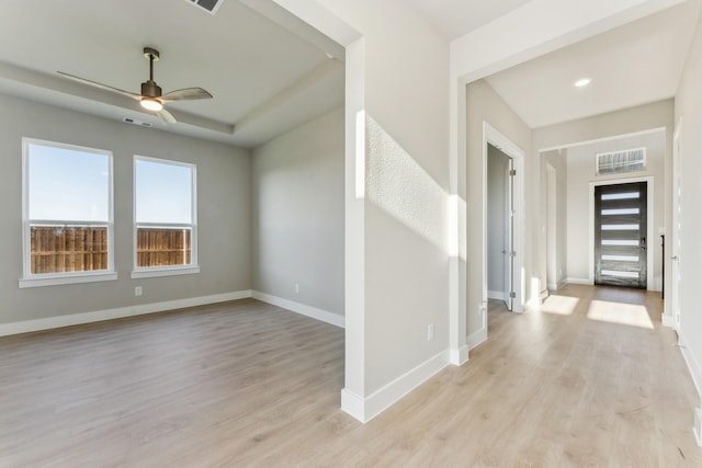 foyer with visible vents, a ceiling fan, baseboards, light wood-type flooring, and a tray ceiling