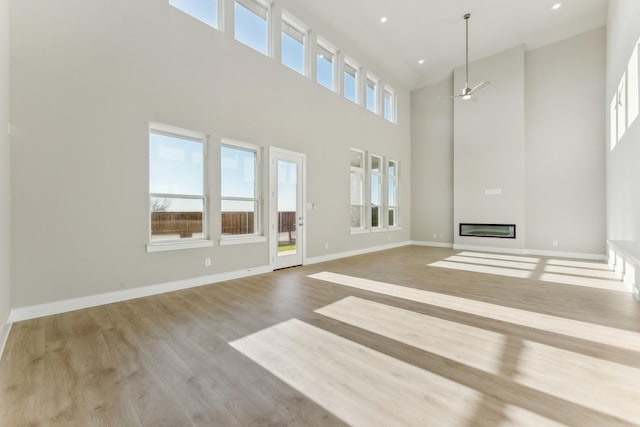 unfurnished living room featuring a towering ceiling, light hardwood / wood-style floors, and ceiling fan