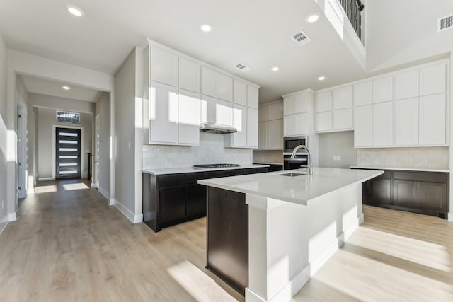 kitchen featuring a center island with sink, gas stovetop, white cabinetry, and sink