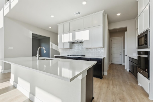 kitchen with oven, white cabinetry, and an island with sink