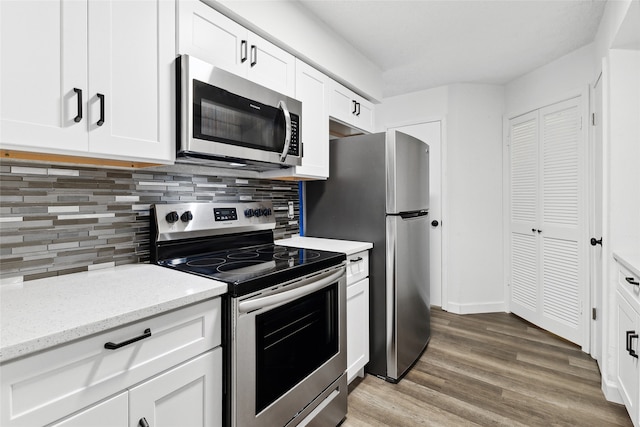 kitchen featuring decorative backsplash, hardwood / wood-style floors, stainless steel appliances, light stone countertops, and white cabinetry