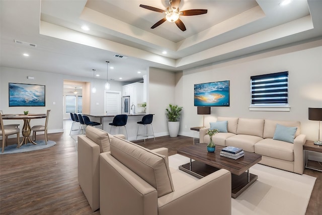 living room featuring hardwood / wood-style floors, a tray ceiling, ceiling fan, and sink