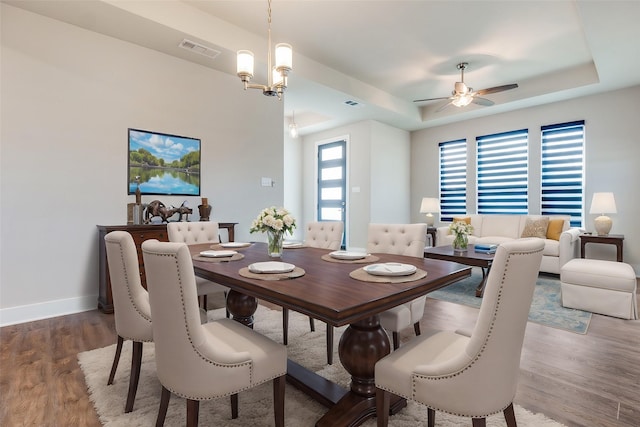 dining area featuring hardwood / wood-style flooring, ceiling fan with notable chandelier, a healthy amount of sunlight, and a raised ceiling