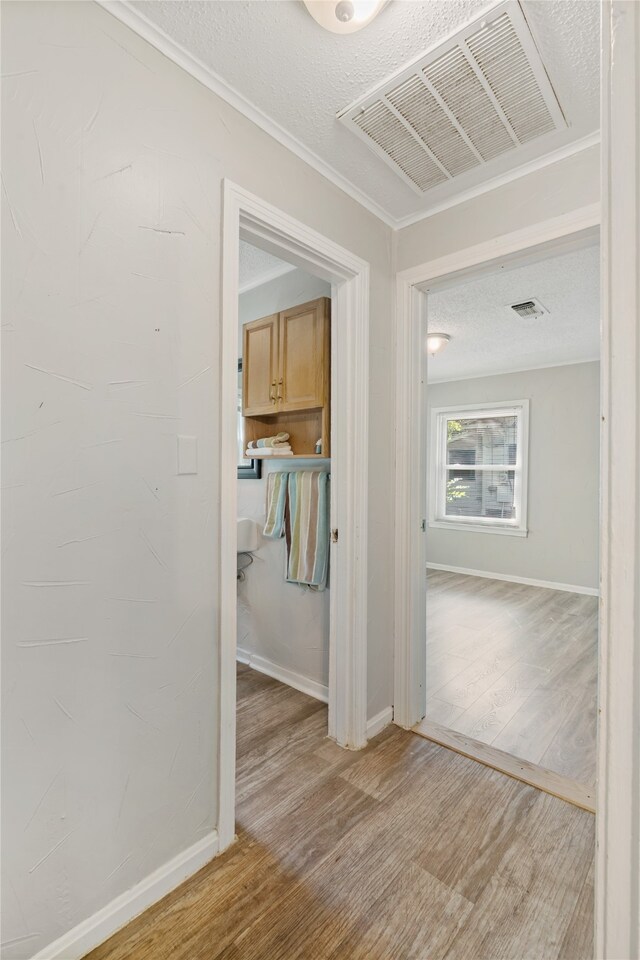 corridor featuring ornamental molding, light wood-type flooring, and a textured ceiling