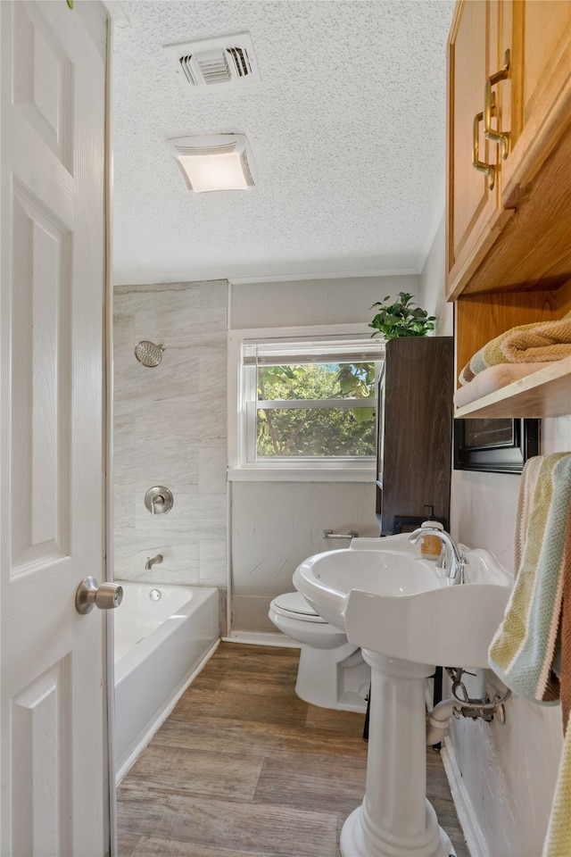 bathroom featuring wood-type flooring, toilet, a textured ceiling, and shower / bath combination