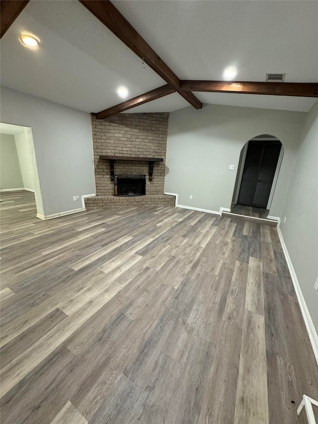 unfurnished living room featuring a brick fireplace, vaulted ceiling with beams, and hardwood / wood-style floors