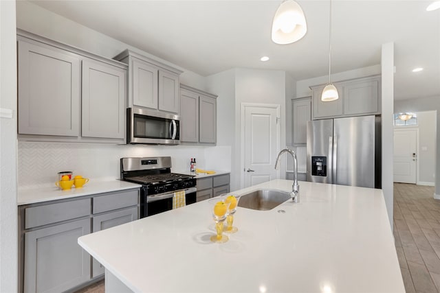 kitchen featuring sink, an island with sink, pendant lighting, gray cabinets, and appliances with stainless steel finishes