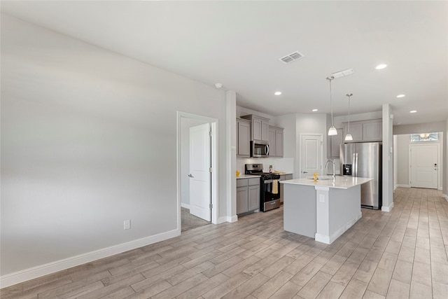 kitchen featuring stainless steel appliances, gray cabinets, light hardwood / wood-style floors, and an island with sink