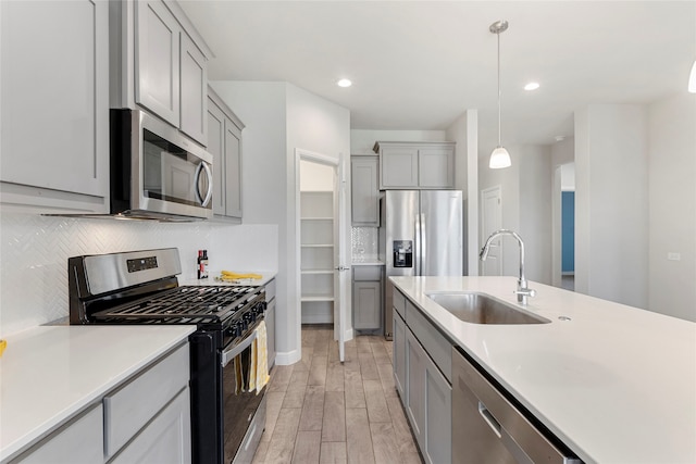 kitchen with sink, light hardwood / wood-style flooring, backsplash, decorative light fixtures, and appliances with stainless steel finishes