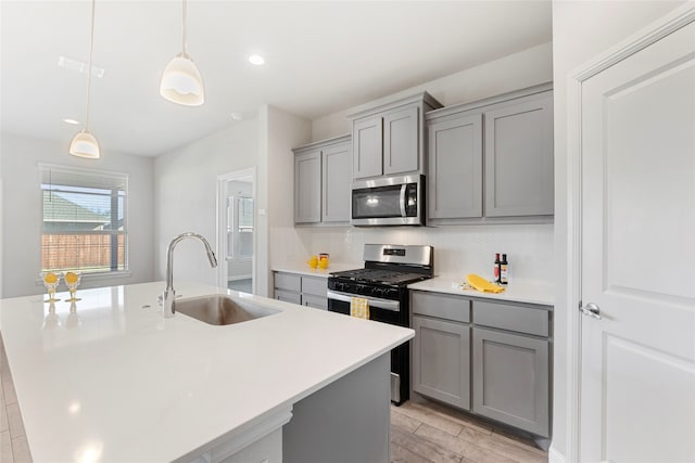 kitchen with light wood-type flooring, stainless steel appliances, a kitchen island with sink, sink, and decorative light fixtures