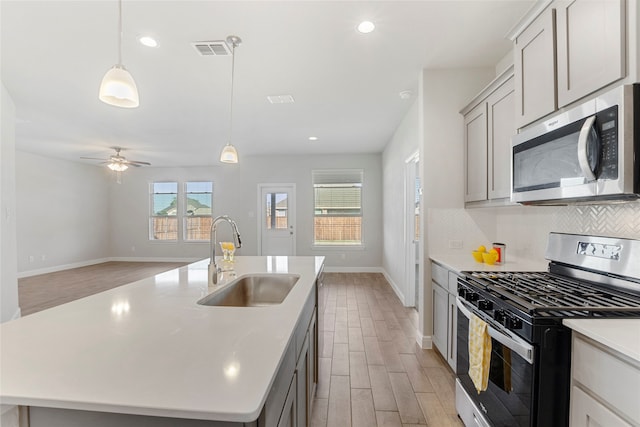 kitchen with gray cabinetry, sink, stainless steel appliances, a center island with sink, and light wood-type flooring