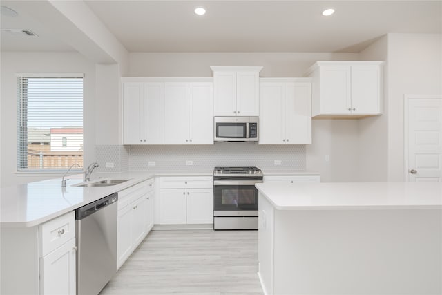 kitchen with appliances with stainless steel finishes, sink, light hardwood / wood-style floors, white cabinets, and decorative backsplash