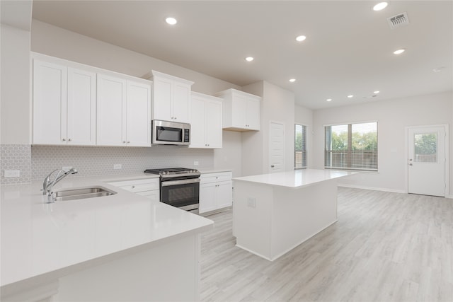 kitchen featuring sink, a kitchen island, stainless steel appliances, white cabinets, and light hardwood / wood-style flooring